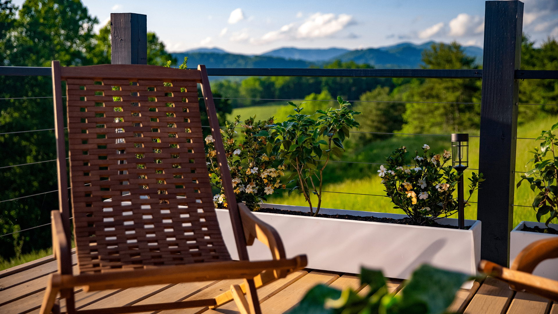 Wooden lounge chair on a deck at golden hour looking out to Blue Ridge mountains and white blossoms